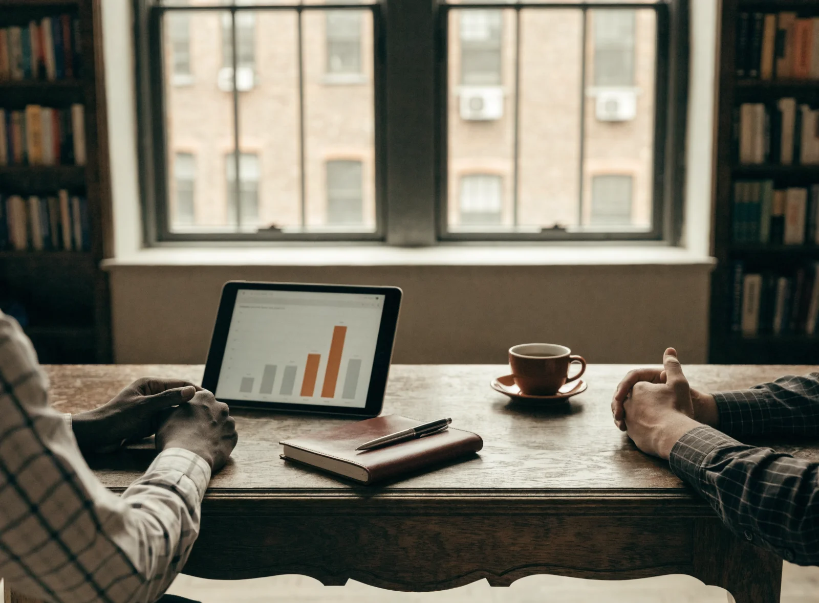 A tablet on a partner's desk showing a bar chart beside a leather notebook and pen