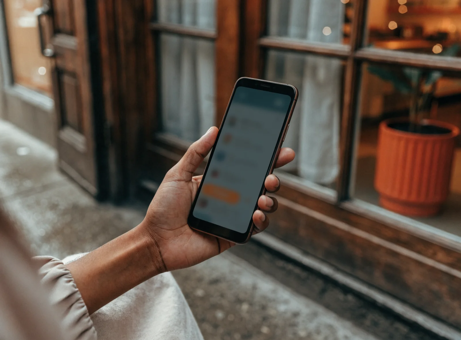 A hand holding a phone on a sidewalk showing a local search result