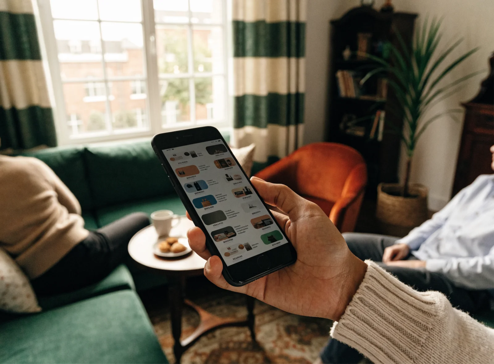 A hand holding a phone showing a row of shopping ad tiles