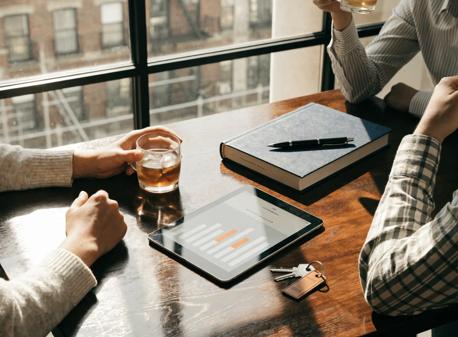 A tablet on a desk showing a bar chart beside house keys and a folder